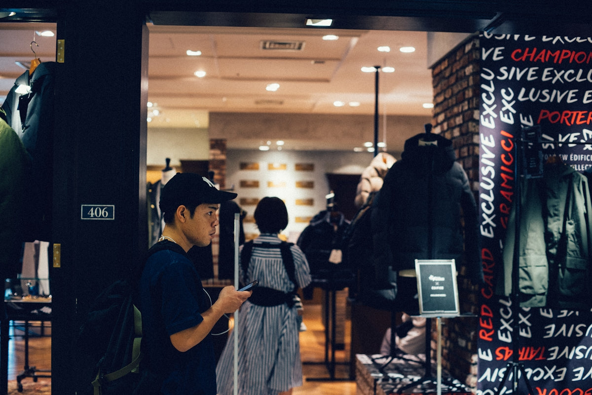 man in blue shirt standing by the store entrance fiddling on his phone